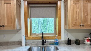 Una cocina con armarios de madera, un lavamanos de acero inoxidable y una ventana con vistas a árboles.