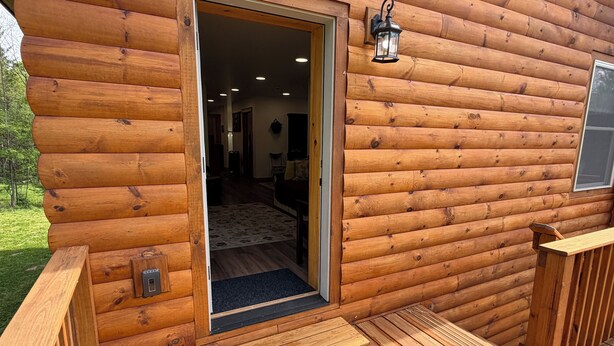 Una cabaña de madera con una puerta que da a un interior con alfombra, un banco y un felpudo.