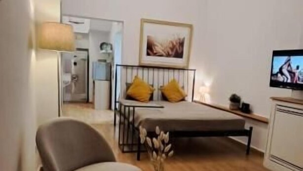 Um espaço compacto para viver, com sofá, mesinha redonda, cadeira, cama, televisão e um quadro na parede.