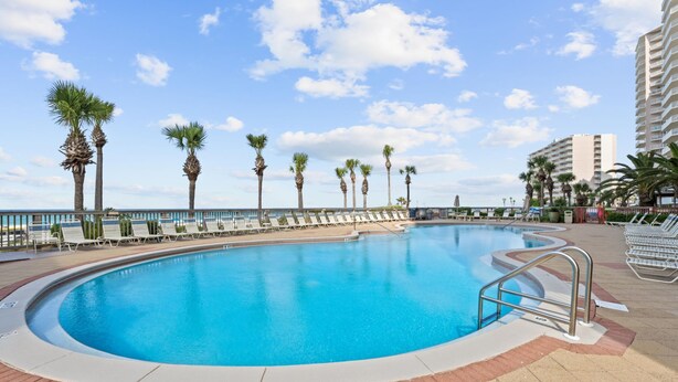 Ein Swimmingpool mit Liegestühlen, Palmen und blauem Himmel.