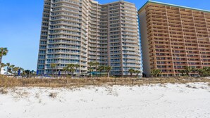 Ein Hotel direkt am Strand mit mehreren Etagen, Balkonen und einem Sandstrand im Vordergrund.