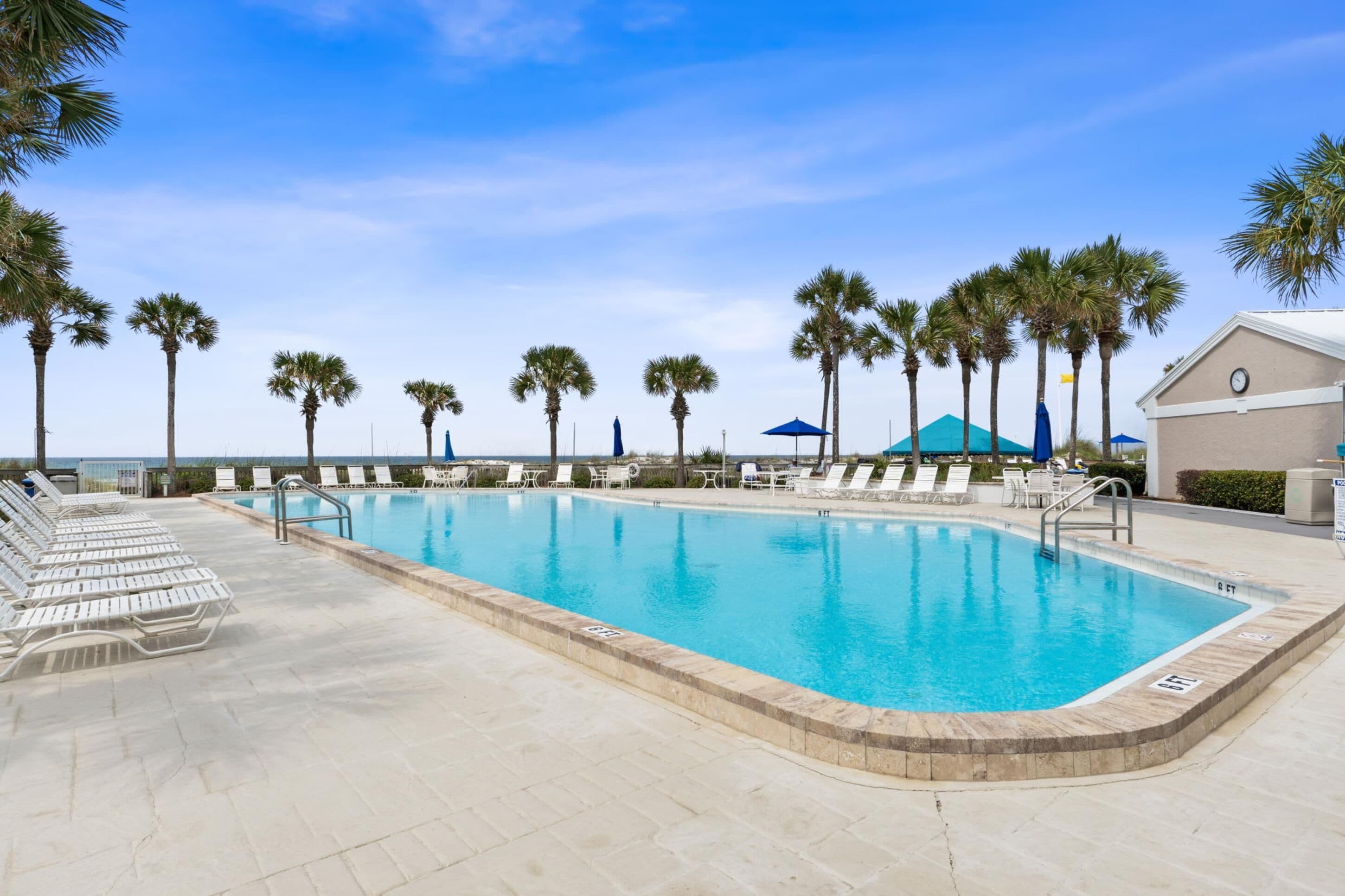 A swimming pool with lounge chairs, palm trees, and a building with a clock.