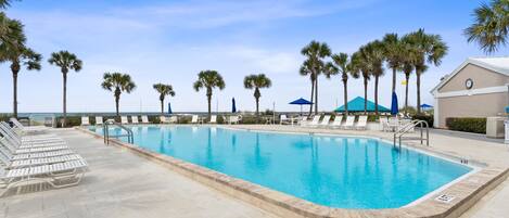 A swimming pool with lounge chairs, palm trees, and a building with a clock.