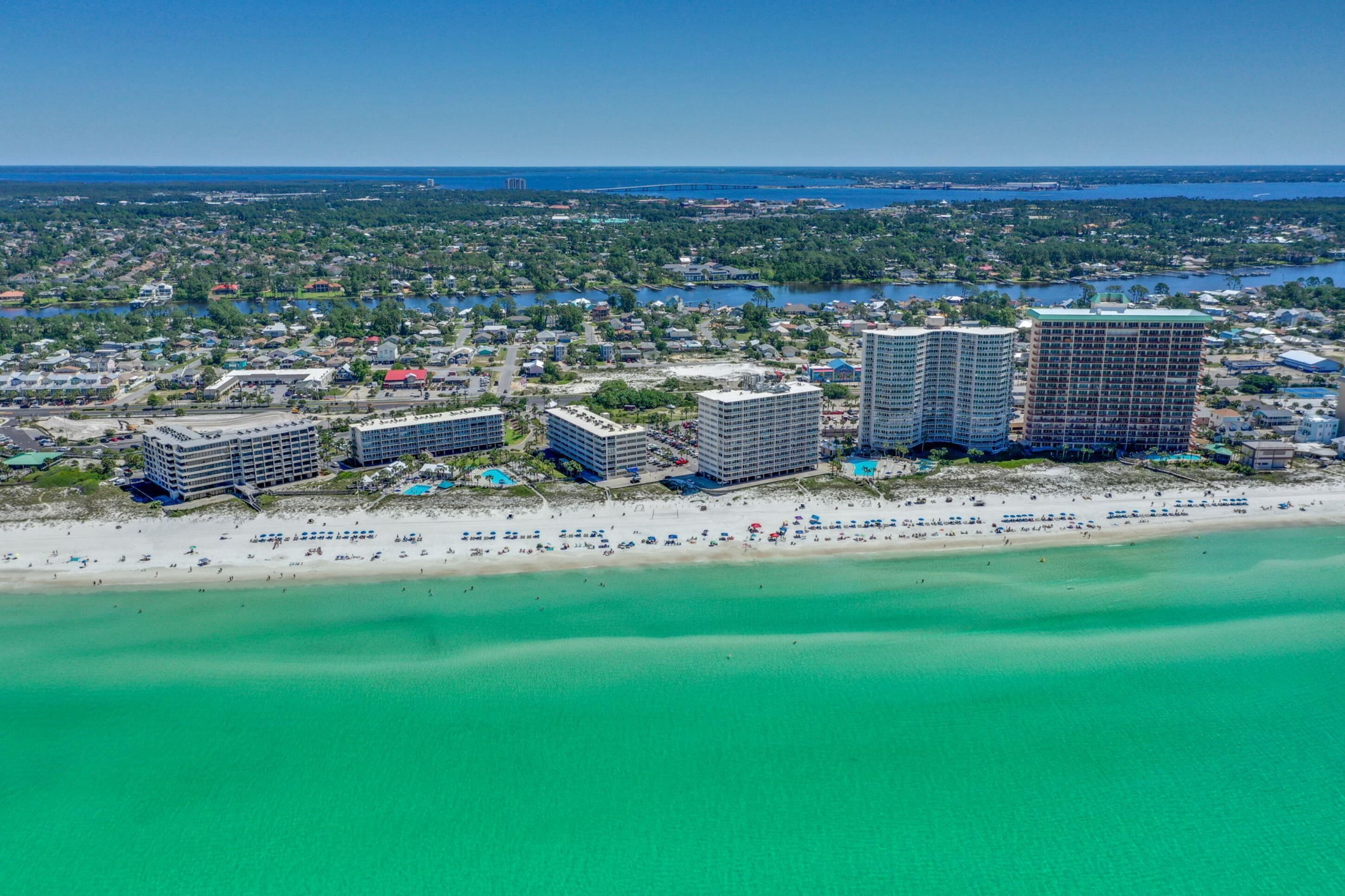 An aerial view of a coastal area with a beach, several high-rise buildings, and a marina.
