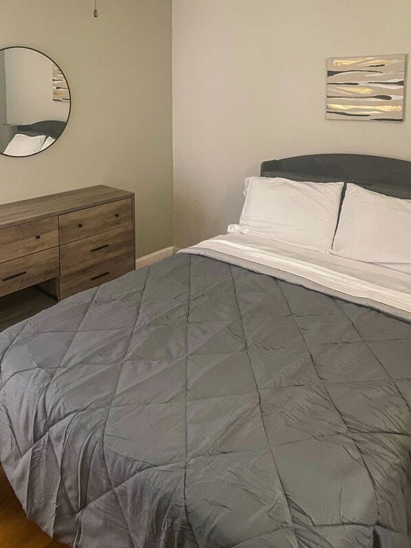 A bedroom with a bed, a dresser, a mirror, and a wall art piece.