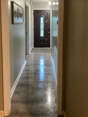 A hallway with a polished wooden floor, a dark door with a glass window, and a 'Welcome' sign on the wall. - Staysobrio Luxury Stays (Gastonia)