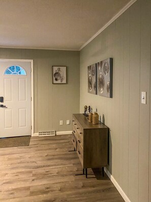 Ein Zimmer mit Holzboden, einer weißen Tür, einem Schmuckstück und Wandbildern.