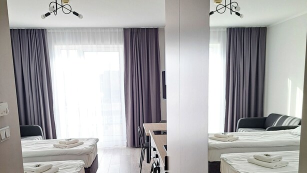 A hotel room with two beds, a desk, a chair, and a large window with curtains. - Sympo Apartaments (Kraków)