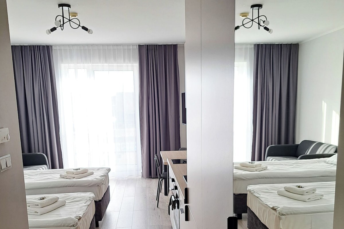 Ein Hotelzimmer mit zwei Betten, einem Schreibtisch, einem Stuhl und einem großen Fenster mit Vorhängen.