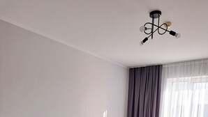 A hotel room with two beds, a headboard, a window with curtains, and a ceiling light fixture. - Sympo Apartaments (Kraków)