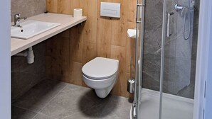 A modern bathroom with a wooden panel wall, a glass shower enclosure, a white sink, and a toilet. - Sympo Apartaments (Kraków)