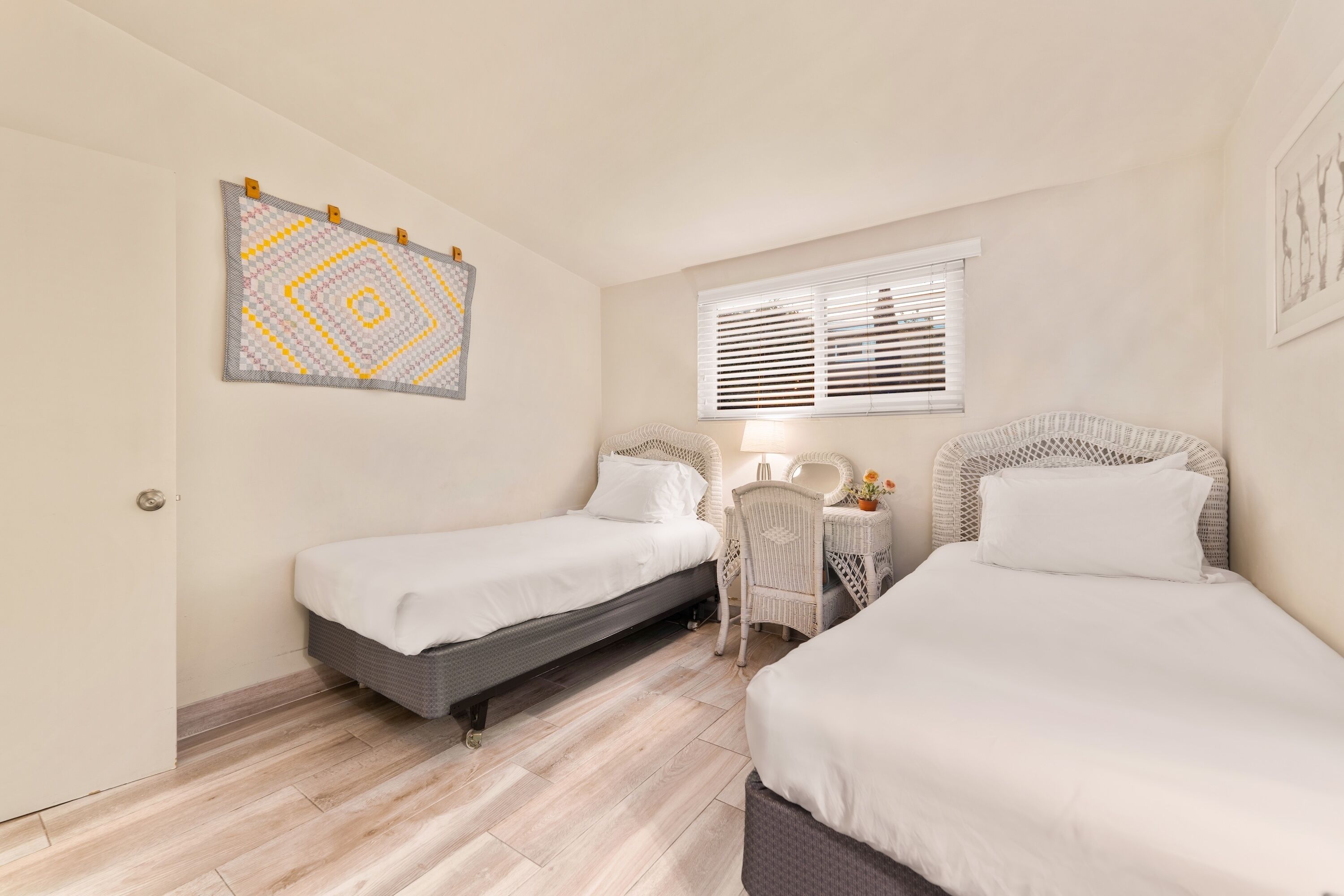 A hotel room with two beds, a small table, a chair, and a window with blinds.