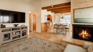 Un salon doté d’une cheminée, d’un téléviseur, d’un coin repas et d’une cuisine visible à travers une porte ouverte.