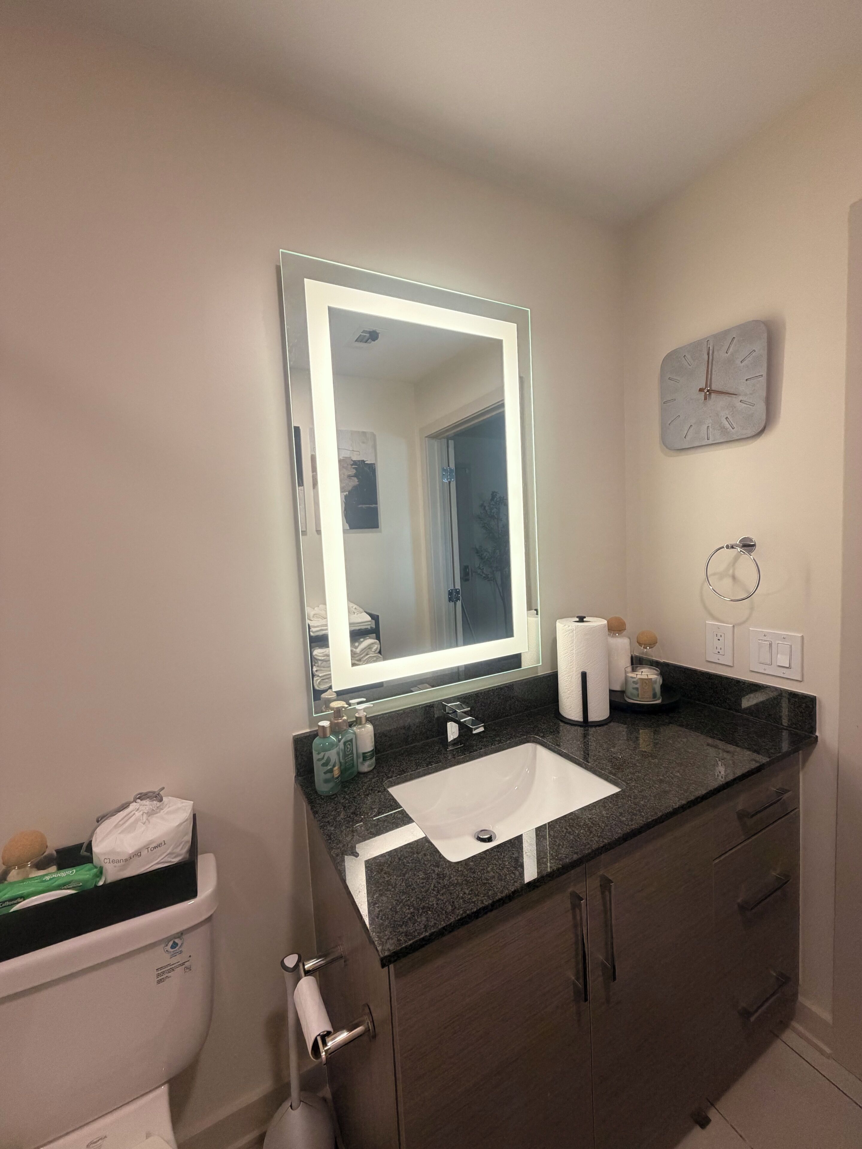 A bathroom with a sink, mirror, clock, and toiletries.