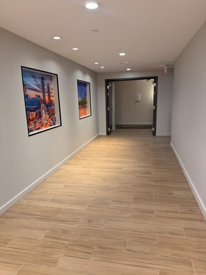 A hallway with wooden flooring, recessed ceiling lights, and framed cityscape artwork on the walls. - Cozy 2-bedroom High-Rise apt in Downtown Atlanta w/pool, gym, & rooftop access. (Atlanta)