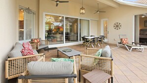 An outdoor patio with wicker furniture, ceiling fans, and a glass door leading to an interior space. - Upscale 4-bedroom house in peaceful Naples with cool AC, Pool, and Spa (Naples)