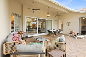 Eine Terrasse im Freien mit Korbmöbeln, Deckenventilatoren und einer Glastür zu einem Innenraum.