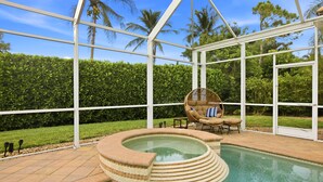 A glass-enclosed pool area with a hot tub, surrounded by a white metal frame, palm trees, and a hedge. - Upscale 4-bedroom house in peaceful Naples with cool AC, Pool, and Spa (Naples)
