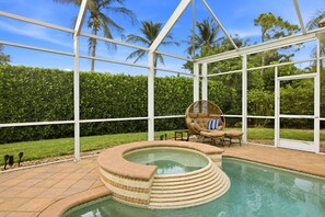 Ein Poolbereich mit Glasumrandung und Whirlpool, umgeben von einem weißen Metallgestell, Palmen und einer Hecke.