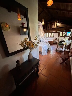 A rustic interior with a wooden bench, a vase of flowers, a mirror, and a bed with a canopy. - Lenna por GEstores (Huasca De Ocampo)