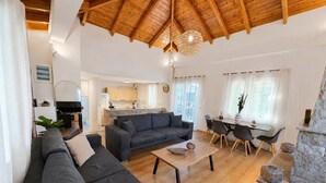 A spacious living area with a high wooden ceiling, a sofa set, a dining table, and a kitchen in the background. - Villa Mare Lechaio - A Beachside Hideaway (Lechaio)