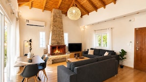 A spacious living room with a stone fireplace, a large sofa, a dining area with a table and chairs, and a television. - Villa Mare Lechaio - A Beachside Hideaway (Lechaio)