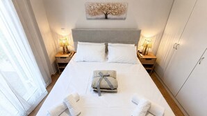 A neatly made bed with white linens, two bedside lamps, a folded towel, and a wall-mounted artwork. - Villa Mare Lechaio - A Beachside Hideaway (Lechaio)