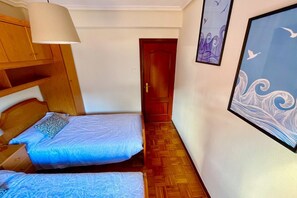 Ein kleines Zimmer mit zwei Betten, einem Holzschrank, einer Tür und Wandbildern.