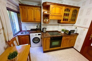 Cocina compacta con armarios de madera, lavadora, microondas y pileta.