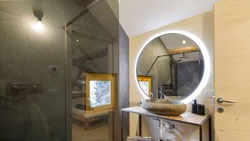 Un bagno moderno con cabina doccia in vetro, mobile lavabo in legno e lavandino in pietra, oltre a un grande specchio con illuminazione integrata.
