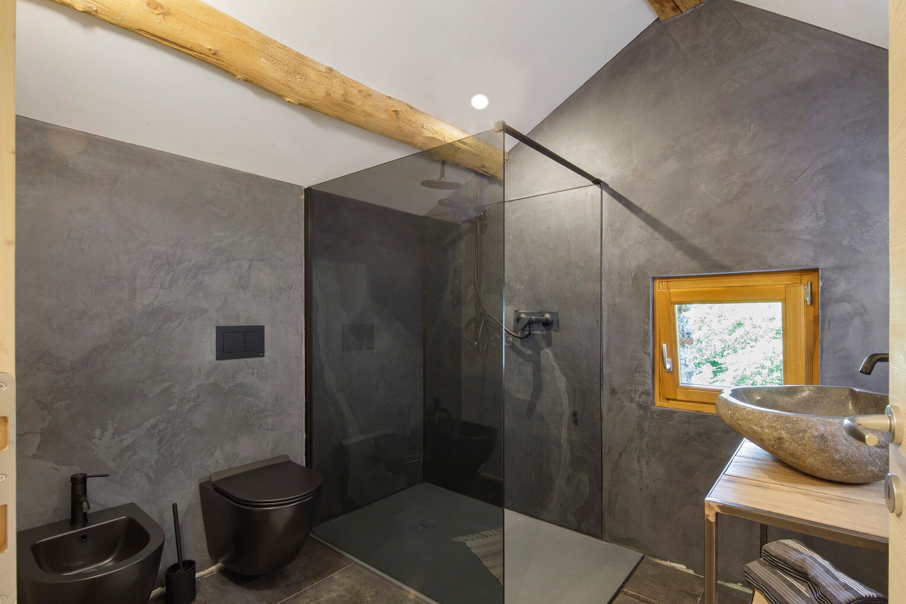 A modern bathroom with a glass-enclosed shower, a wooden-framed window, and a stone sink.