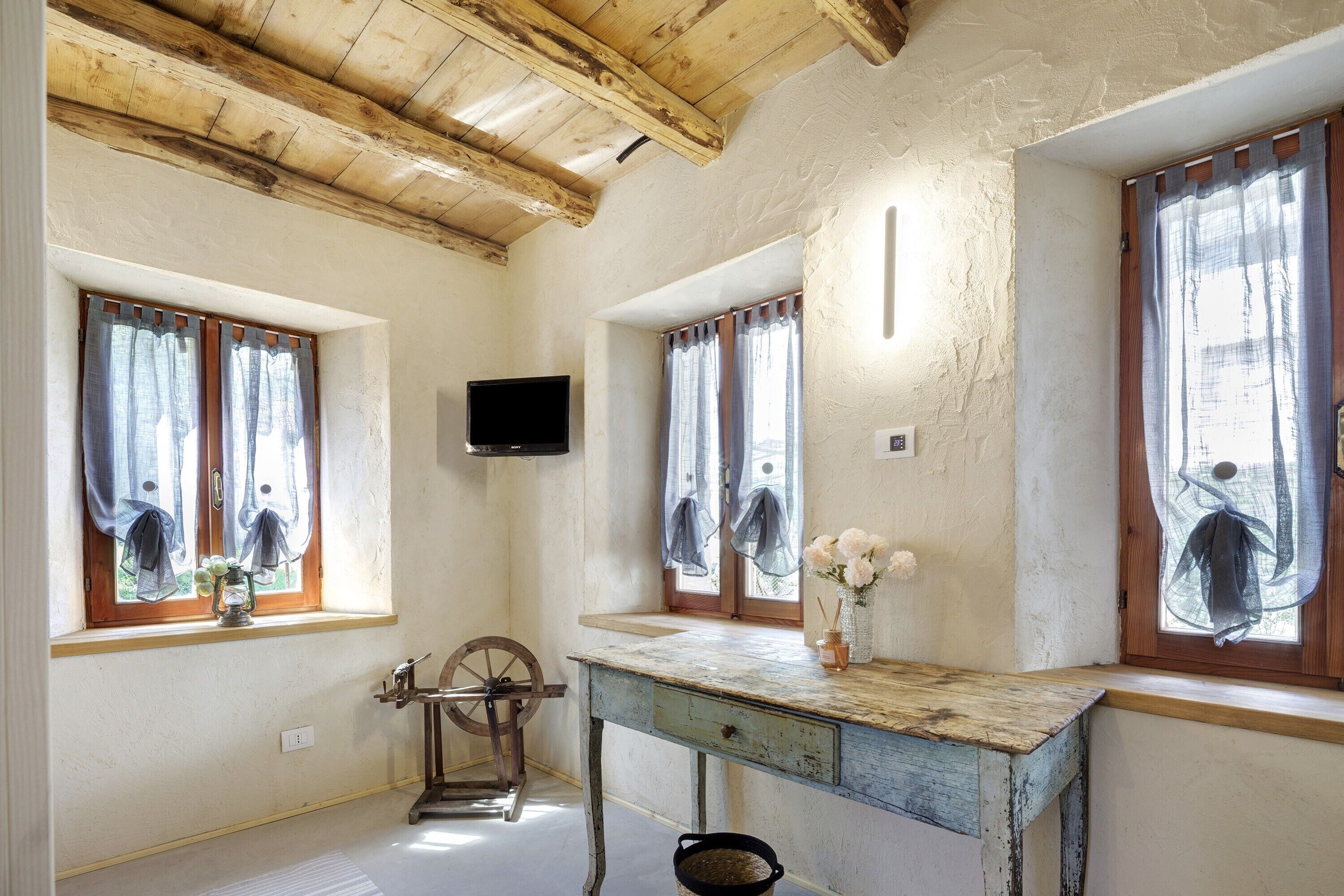 Una stanza rustica con travi in legno, una rocchetto, un tavolo d'epoca e un televisore montato a parete.