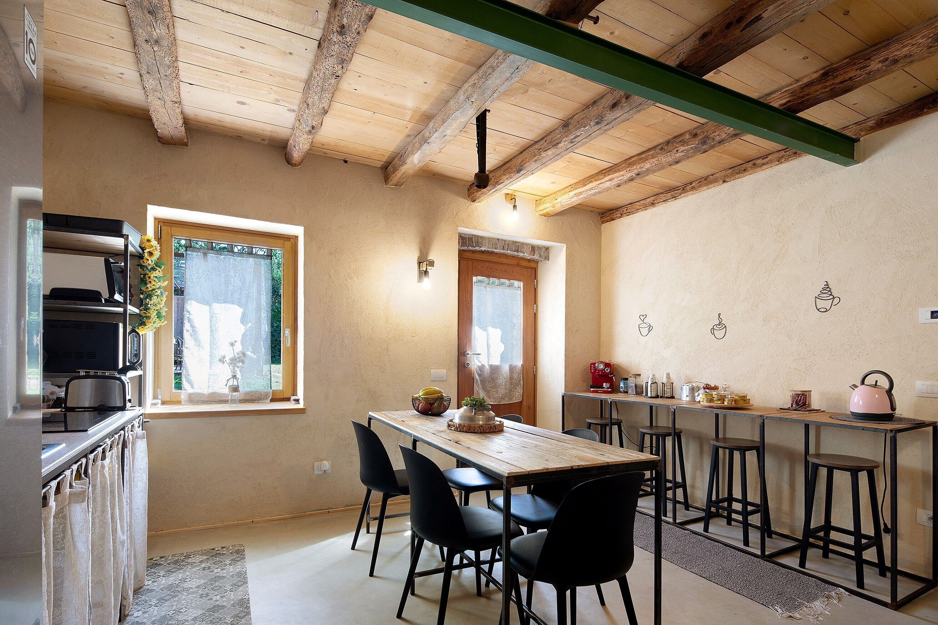 A kitchen with a wooden ceiling, a dining table with chairs, a microwave, and a coffee machine.