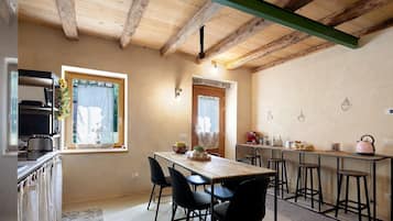 A kitchen with a wooden ceiling, a dining table with chairs, a microwave, and a coffee machine.