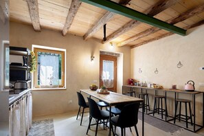 Een keuken met een houten plafond, een eettafel met stoelen, een magnetron en een koffieapparaat.