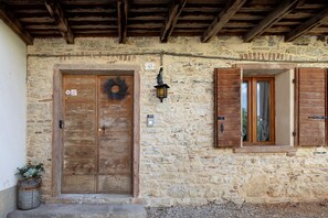 A rustic stone building with a wooden door, a window with shutters, and a lantern on the wall.