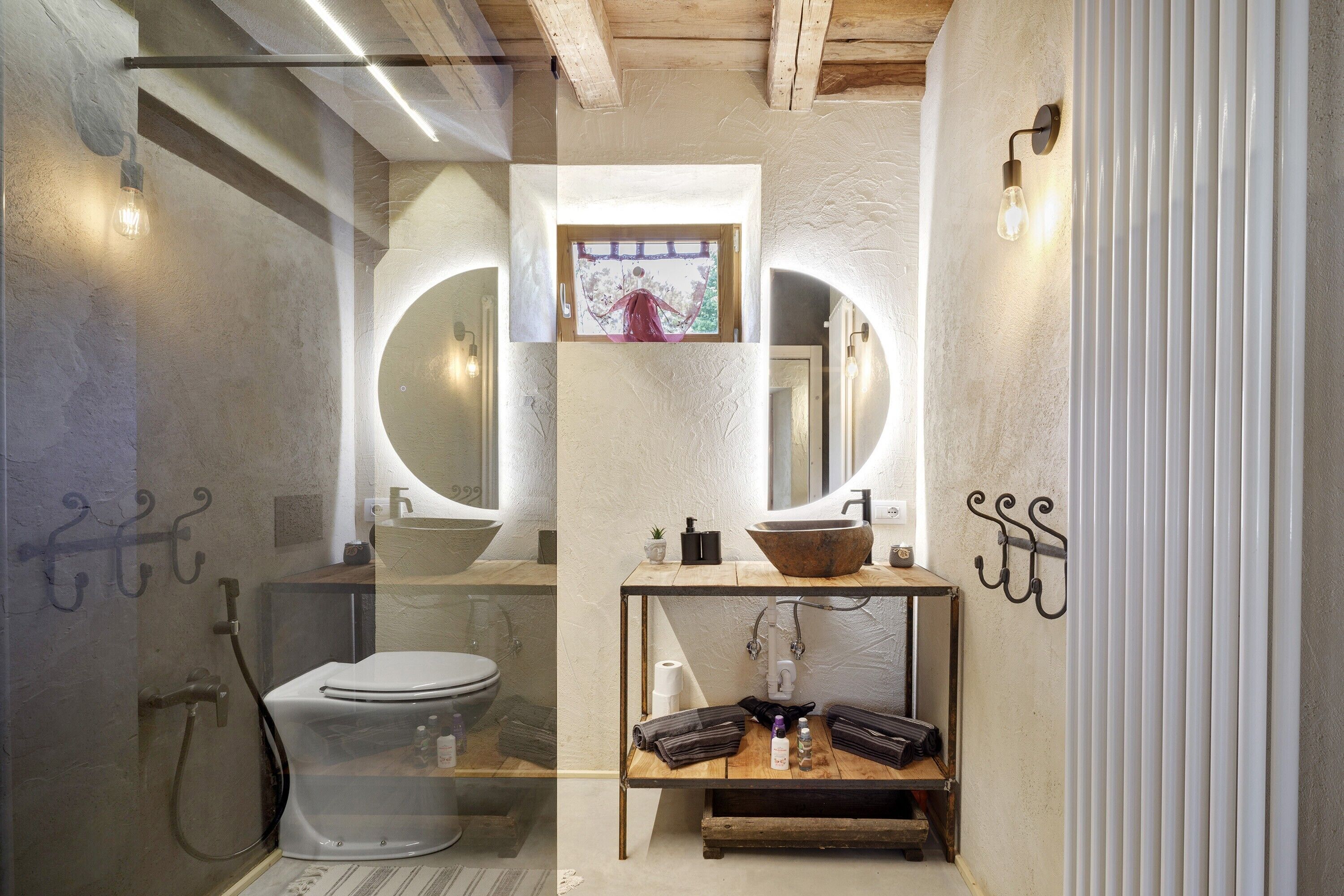 Une salle de bain équipée de toilettes, de deux lavabos, d’un miroir et d’une étagère contenant des articles de toilette.
