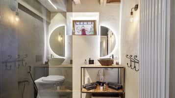 Une salle de bain équipée de toilettes, de deux lavabos, d’un miroir et d’une étagère contenant des articles de toilette.
