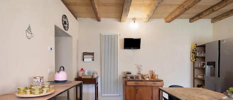 A kitchen with wooden beams, a dining table, chairs, a refrigerator, and a TV mounted on the wall.