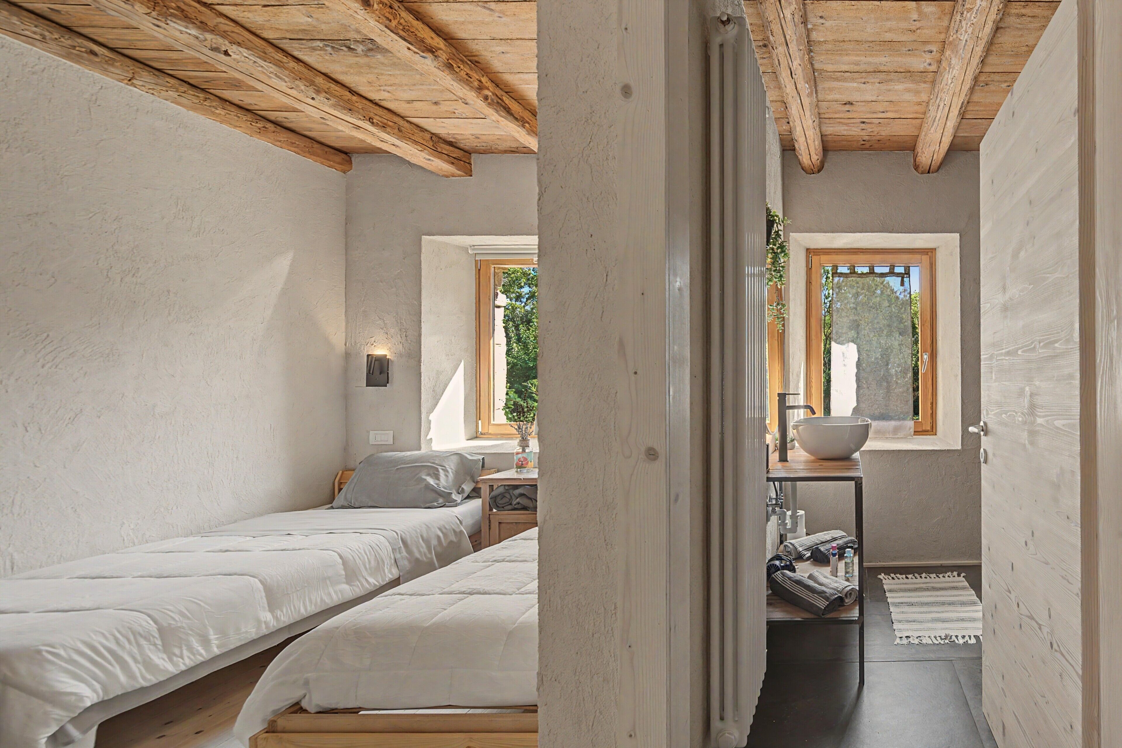 Una camera da letto con due letti, un soffitto in legno, una finestra e un bagno con lavandino.