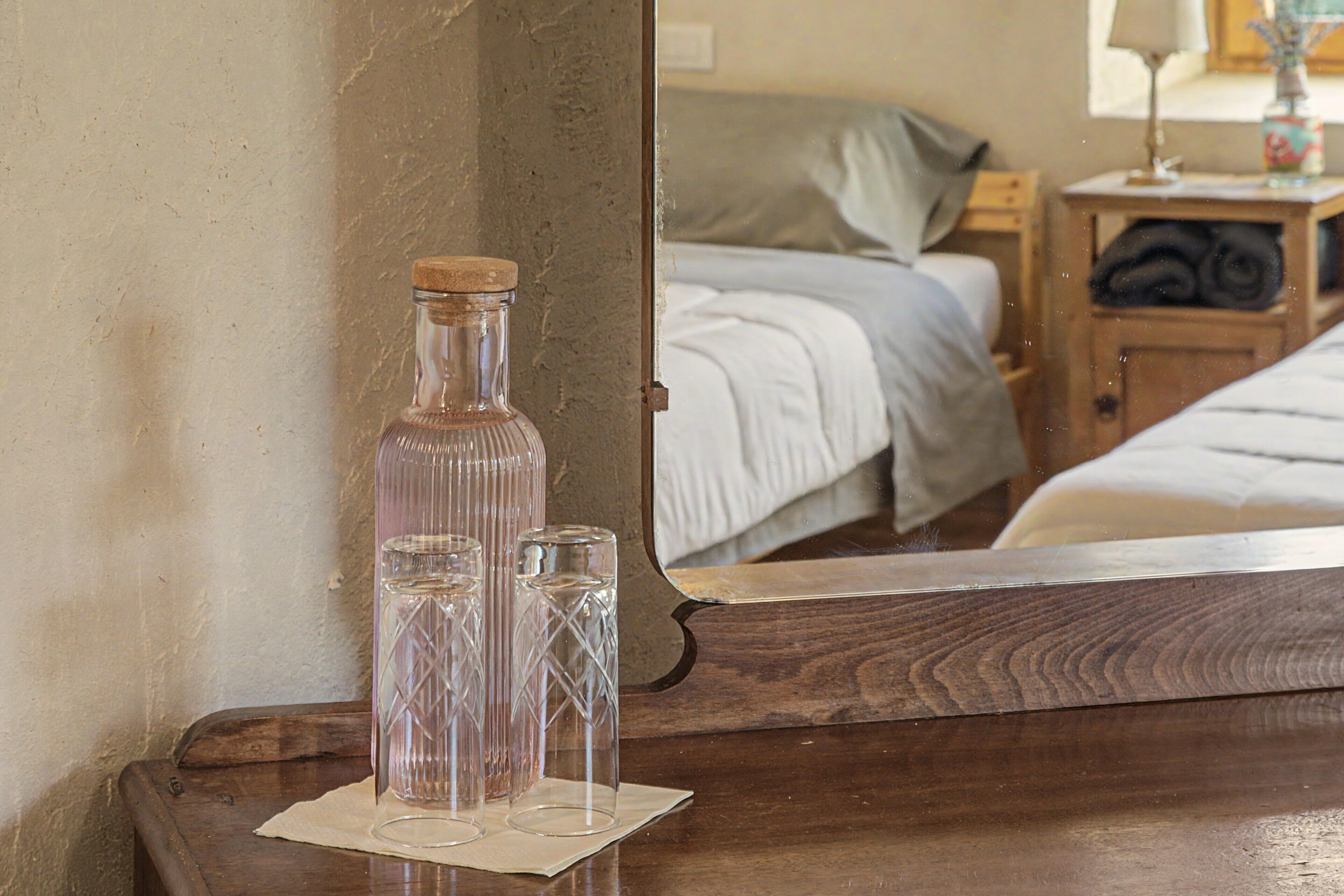 Ein Nachttisch aus Holz mit einer Glasflasche und zwei Gläsern auf einem weißen Tuch.