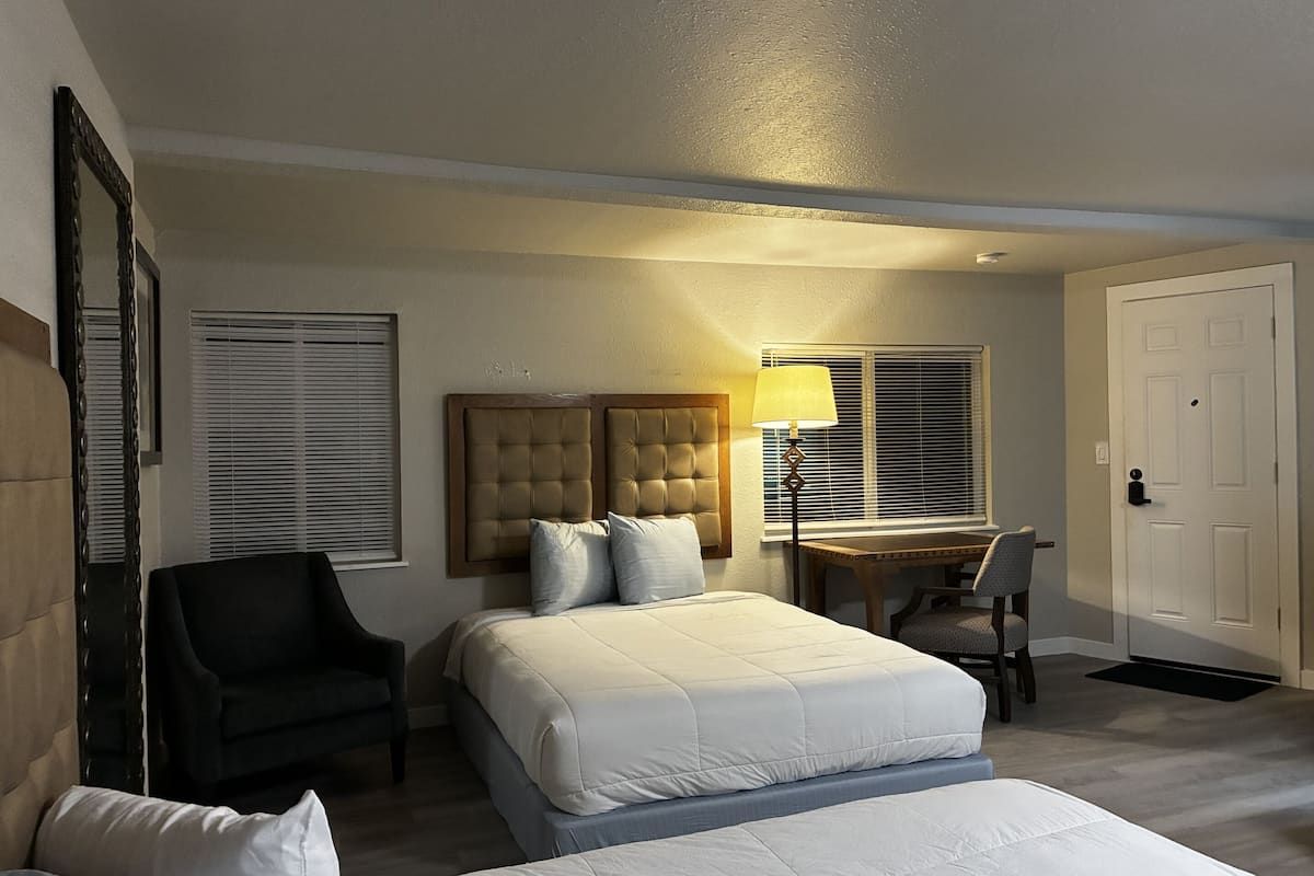 Quarto de hotel com cama, escrivaninha, cadeira, luminária e porta.