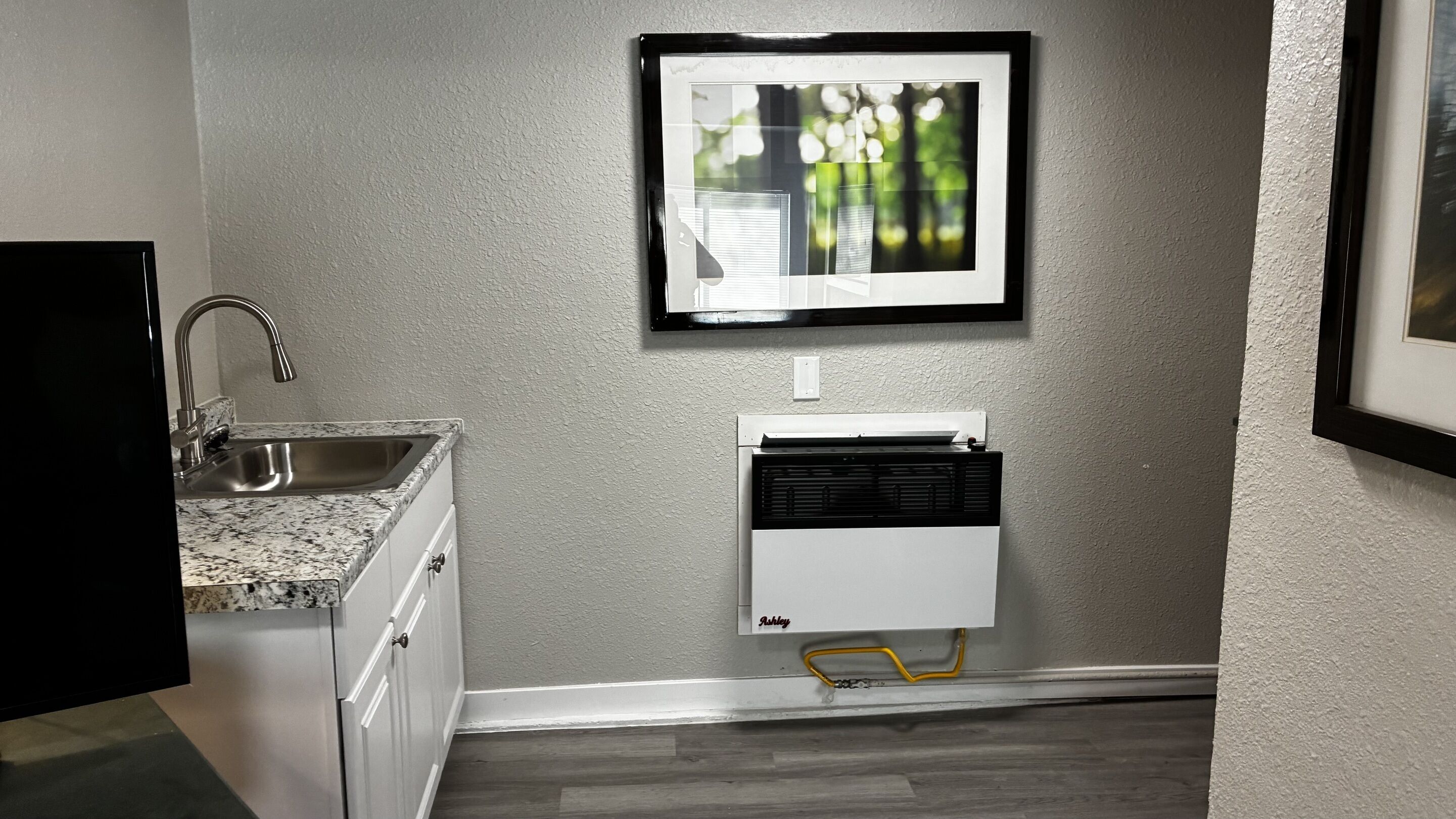 A kitchen with a granite countertop, stainless steel sink, and a wall-mounted air conditioner.