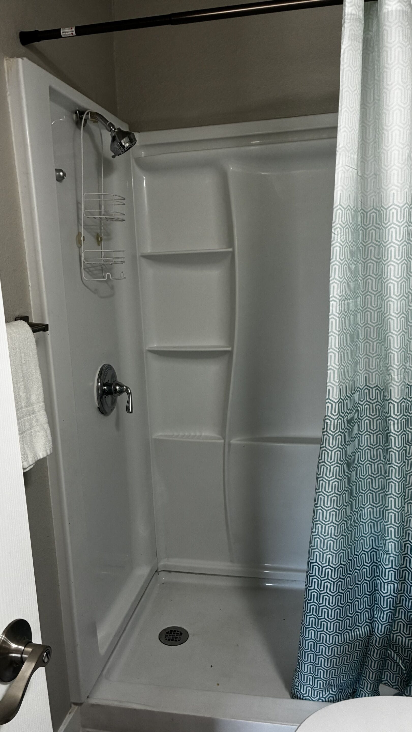 Ducha con puerta blanca, toallero y cortina de ducha.