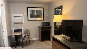 Habitación de hotel con escritorio, silla, televisor, cómoda y un cuadro en la pared.