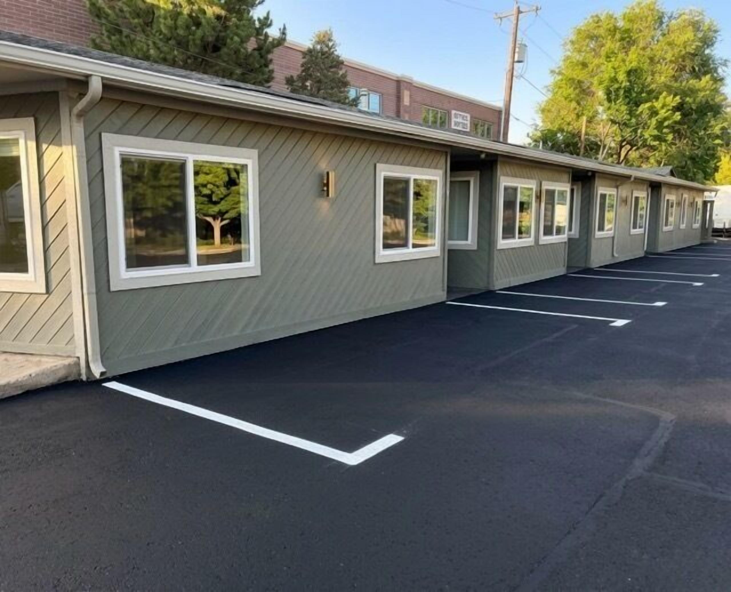 Une rangée de chambres de motel, chacune avec sa propre fenêtre, un parking et un bâtiment en arrière-plan.