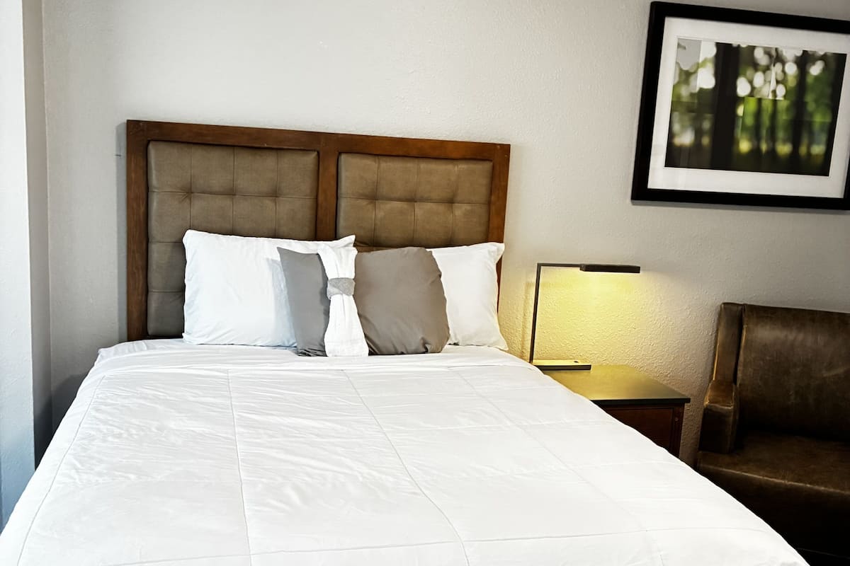 Uma cama bem arrumada com cabeceira de madeira, uma luminária de cabeceira e um quadro na parede.