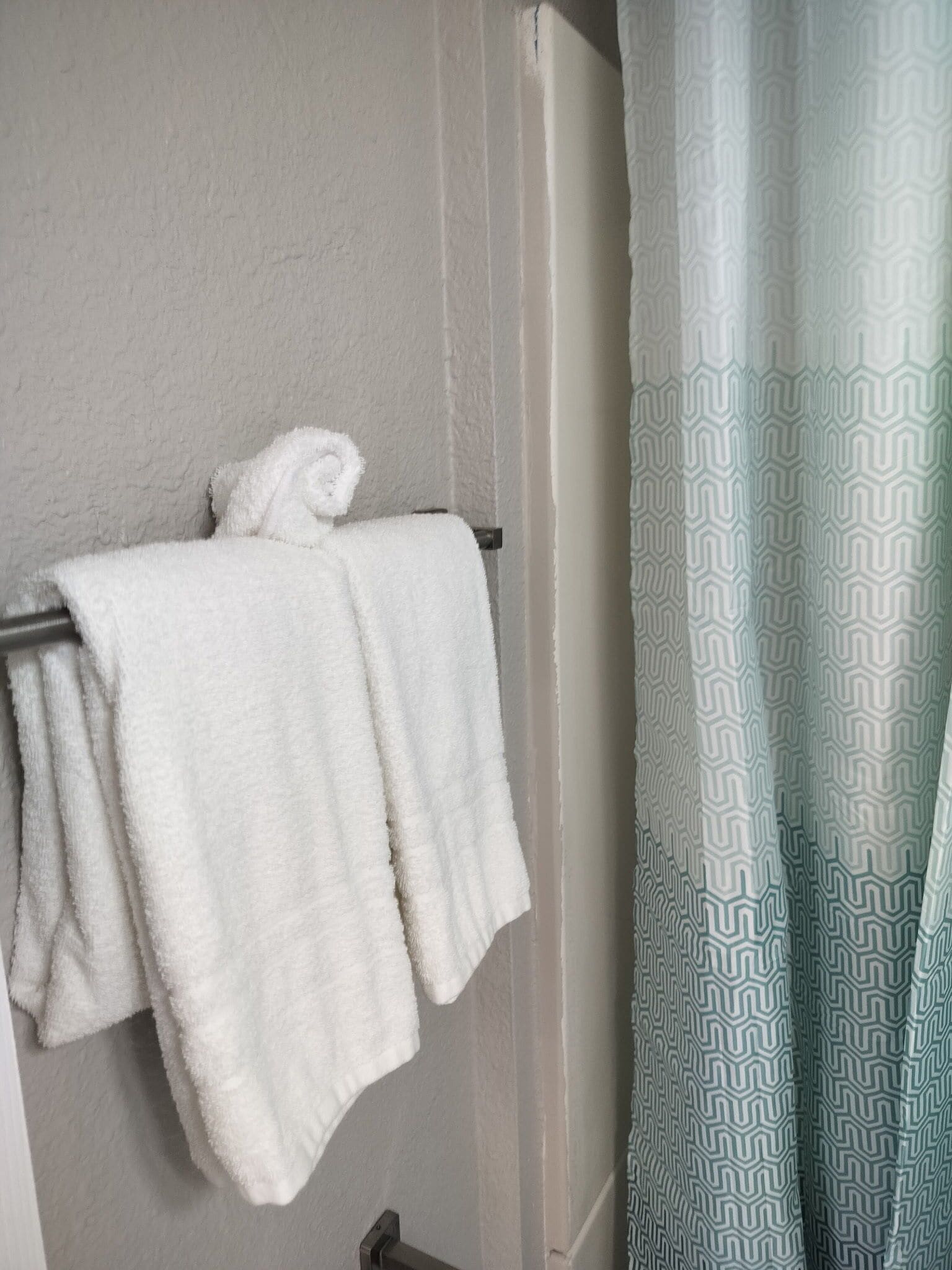 A bathroom with a towel rack holding a folded towel, a patterned shower curtain, and a plain wall.