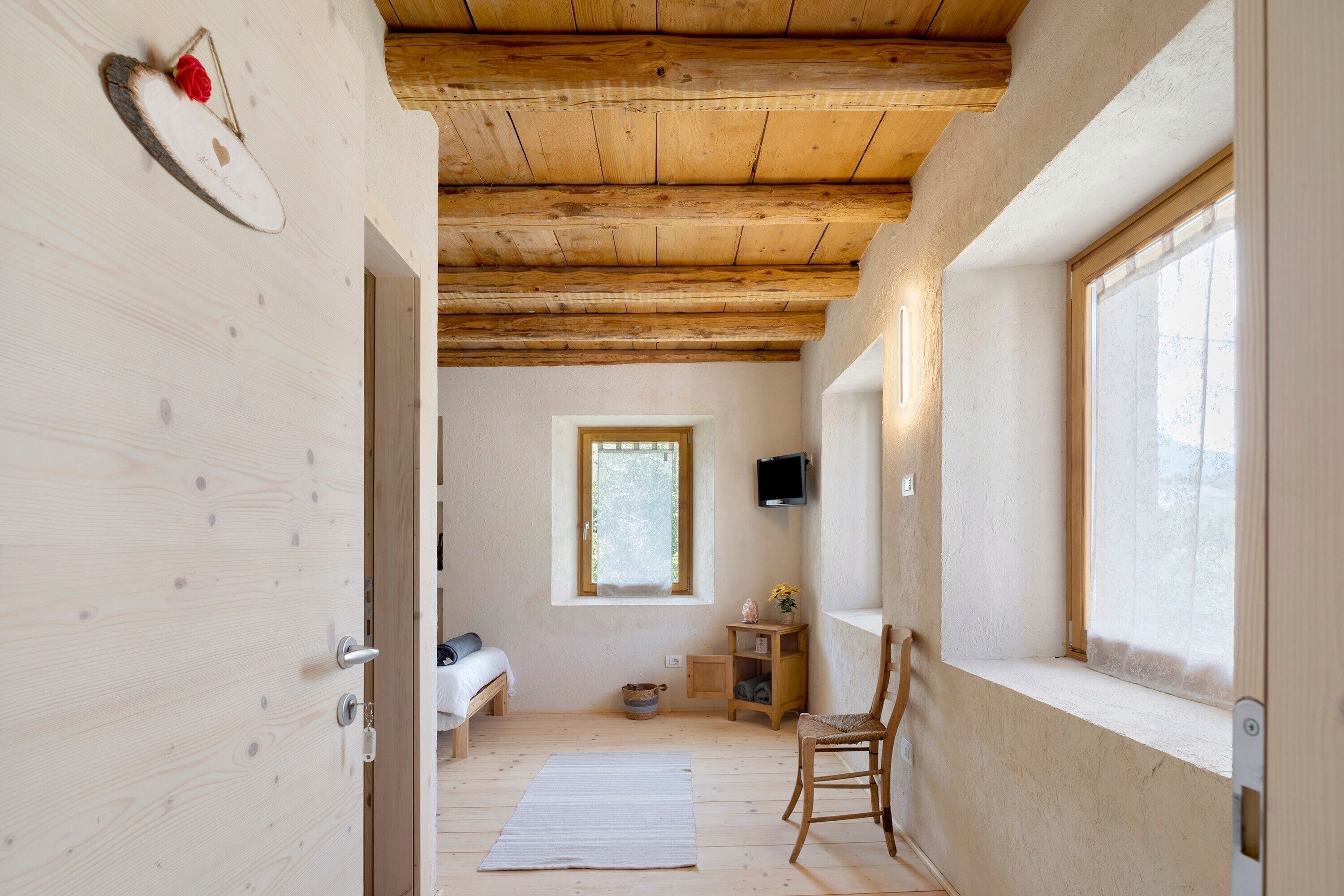 Una habitación con vigas de madera, una cama, una ventana, una silla y una mesita.