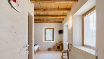 Una habitación con vigas de madera, una cama, una ventana, una silla y una mesita.
